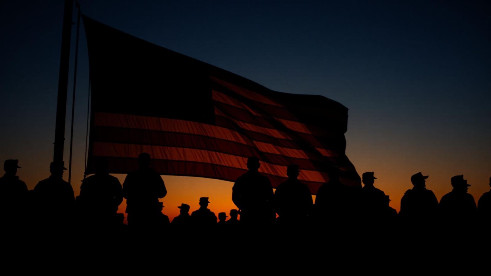 Silhouetted service members standing before an American flag at dusk